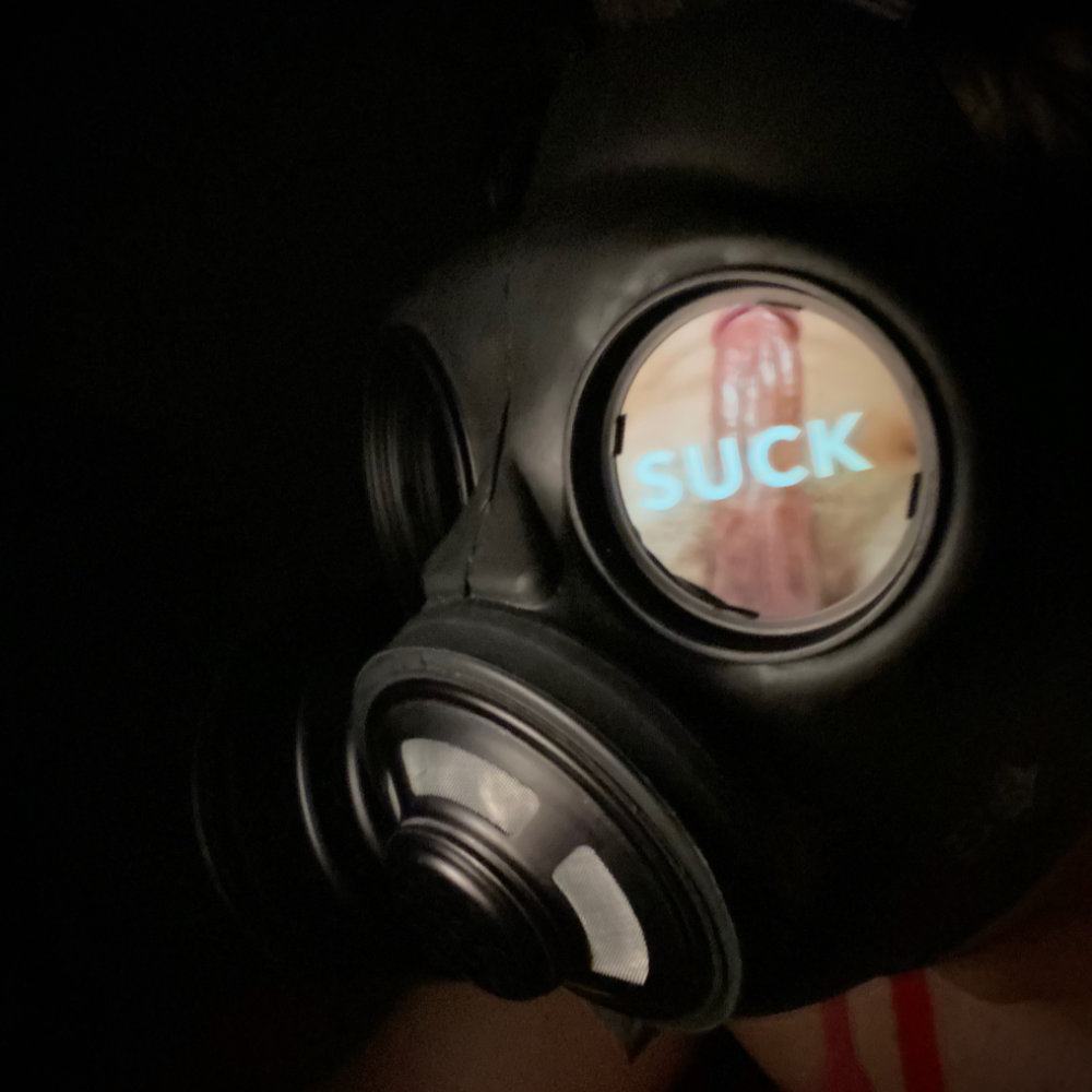Rina in the dark, wearing a gas mask with an image showing a cock with the caption 'suck' reflected in the lens